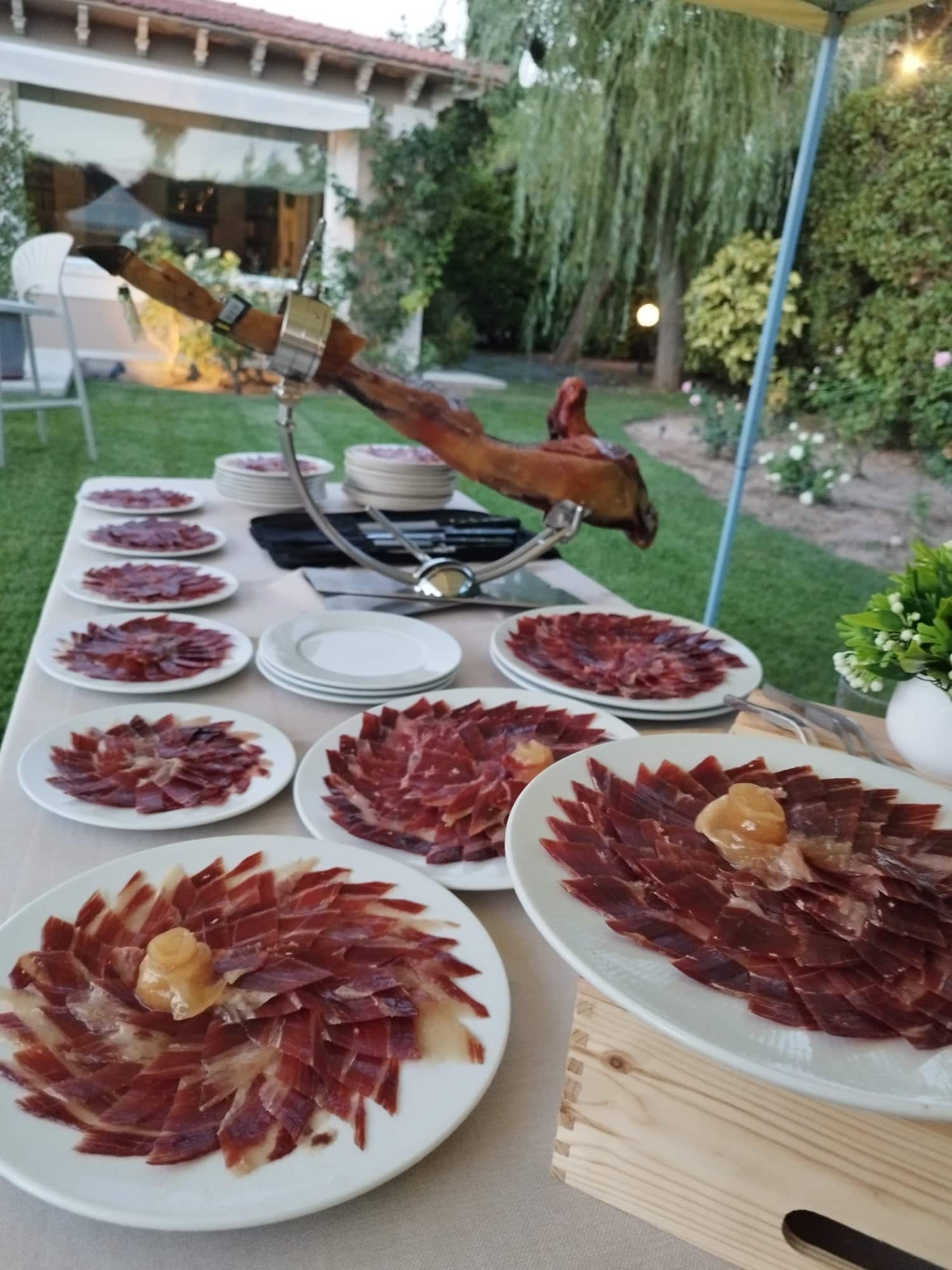 Mesa de platos de jamón ibérico en el jardín de una boda
