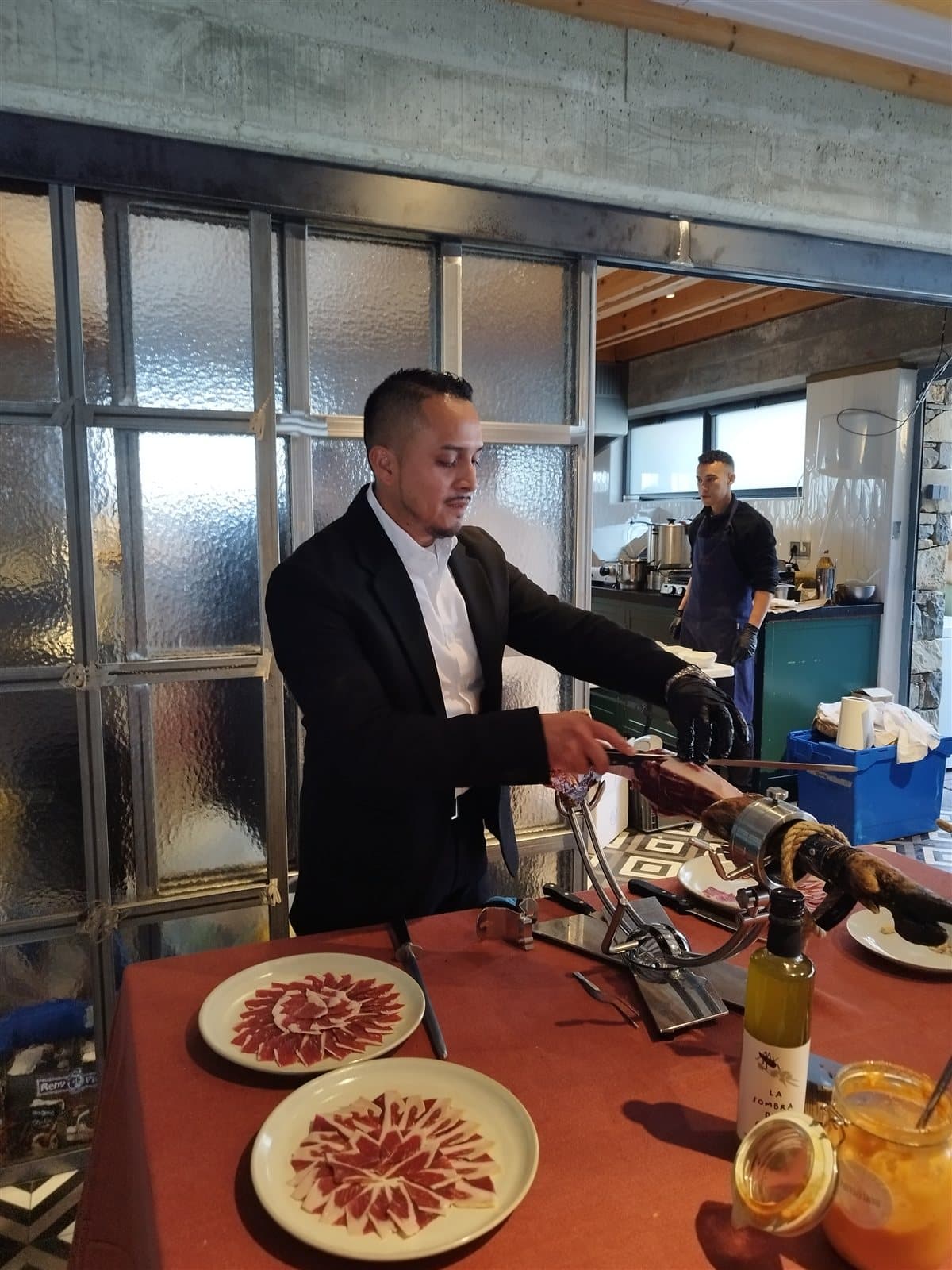 Jeffrey cortando jamón ibérico junto a los platos emplatados para los invitados
